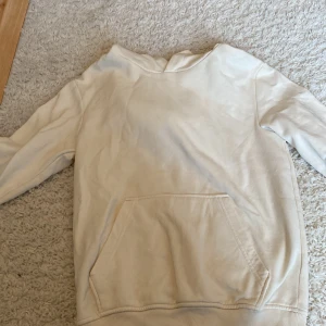 Vit hoodie från KappAhl med ficka - En stilren vit hoodie från KappAhl i storlek 146/152. Tröjan har en klassisk känguruficka framtill, huva och långa ärmar. Perfekt för en chill och avslappnad look. Materialet är mjukt och skönt, troligtvis bomull eller bomullsblandning. 40kr med frakt!👍