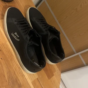 Svarta Saint Laurent sneakers - Svarta sneakers från Saint Laurent med vit sula och handskriven logga på sidan. Skorna har snörning, rund tå och är tillverkade i en mix av skinn och textil. Klassisk och stilren modell som passar till det mesta. Självklart äkta, köpta från trendsellers för 4500 helt nya. Befis finns. Låda medföljer storlek 46. Skriv vid funderingar🙌