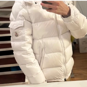 Vit M pufferjacka herr S - Säljer en snygg vit pufferjacka från Moncler med klassisk logga på ärmen och dragkedja framtill. Jackan har quiltad design, fickor med dragkedja och en extra ficka på ärmen. Perfekt för kalla dagar och riktigt clean look.