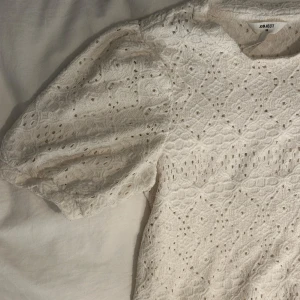 Vit spetsblus från Object XS - Säljer en superfin vit blus/broderad T-shirt från Object i storlek XS. Blusen har korta puffärmar och är täckt av ett broderat spetsmönster med små hål och struktur. 