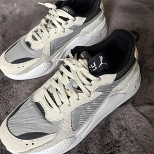 Puma RS-X sneakers i grå och beige - Snygga Puma RS-X sneakers i grått, beige och svart med coola detaljer. Ovandel i mesh och mocka, vita snören och svart innersula. Tjock, vit sula ger en modern look. Perfekta för dig som gillar streetstyle och sportig vibe.