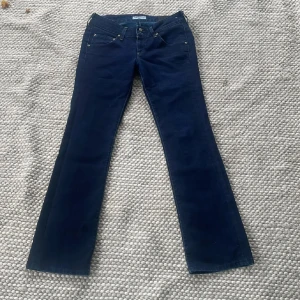 Mörkblå bootcut jeans från Lee - Snygga mörkblå jeans från Lee med klassisk femficksdesign och bootcut-ben lågmidjade. Midjemått ca 39 cm innerbenslängd ca 80 cm. Enda defekten är lite slitna långst ner men syns knappt när man har dem på sig. Köpta för ca 1900 kr.