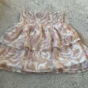 Beige och vit volangkjol KappAhl - Supersöt kortkjol från KappAhl i beige och vitt med abstrakt mönster. Kjolen har bred smock i midjan och dubbla volanger som ger en flowig känsla. Perfekt för dig som gillar en luftig och trendig stil.