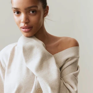 V-Ringad Stickad kofta  - Superfin beige kofta från H&M i croppad modell med v-ringning och stora knappar framtill. Mjuk och skön, perfekt att slänga över en topp. Långärmad och med ribbade muddar för extra stilpoäng.