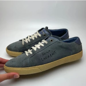 Saint Laurent blå mocka  - Snygga sneakers från Saint Laurent i blå mocka med beige sula och vita snören. Skorna har handskriven logga på sidan och blå detaljer vid hälen. Perfekta för dig som gillar stilrena och exklusiva sneakers med en unik touch.