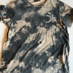 Tie-dye t-shirt från 157, beige/grön - Cool t-shirt från 157 med tie-dye mönster i beige och grön. Tryck med texten 'CREATE. REBUILD' på bröstet. Klassisk rund hals och korta ärmar. Skön bomullskvalitet, perfekt för en avslappnad streetstyle.