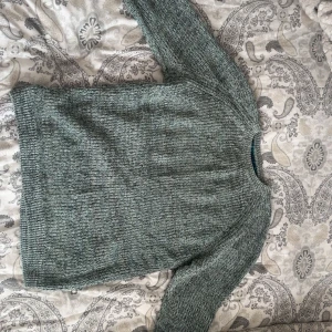 Grönmelerad stickad tröja från STAY - Säljer en grönmelerad stickad tröja från STAY. Tröjan har rund halsringning, långa ärmar och en snygg ribbad kant vid ärmslut och nederkant. Perfekt för lager på lager och chill dagar.