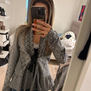 Mönstrad kofta med knytband - Säljer en svartvit kofta med snyggt grafiskt mönster och knytband framtill. Koftan har lång ärm och en lätt utsvängd passform nedtill. Perfekt för lager-på-lager och ger en cool touch till din outfit.