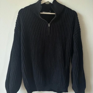 Svart stickad tröja från NA-KD - Ribbstickad svart tröja från NA-KD med hög krage och half zip-dragkedja. Tröjan har långärmad passform och är perfekt för lager-på-lager under kyliga dagar. Snygg och enkel att styla till olika outfits.