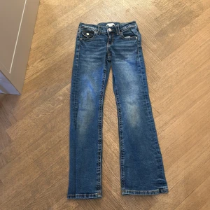 Blå jeans från Gina Tricot, stl 152 - Snygga blå jeans från Gina Tricot i storlek 152. Klassisk femficksmodell med raka ben och coola detaljer som ficklock med knapp bak. Jeansen har en normal passform och är tillverkade i mjukt denimtyg med kontrastsömmar.