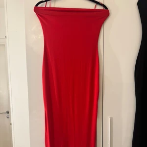 Röd axelbandslös långklänning - Snygg röd långklänning med axelbandslös design. Klänningen har en rak, figurnära passform och en slits baktill.