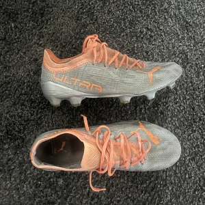 fotbollsskor - Snygga Puma Ultra 1.4 FG/AG fotbollsskor i silver och orange.  I bra skick dobbarna knappt slitna 