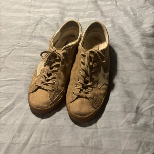 Beige mockasneakers med stjärndetalj - Snygga beige sneakers från Golden Goose i mocka med en ikonisk vit stjärna på sidan och matchande snörning. Skorna har en platt gummisula och silvriga detaljer vid hälen. Inte använda supermycket köpa i Madrid har allt som kom med när man köpte dom.