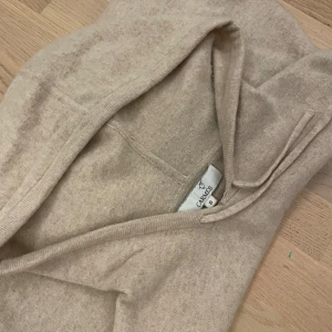 Beige hoodie från Carmès med huva - Säljer en beige hoodie från Carmès i storlek S. Tröjan har huva med snörning och är långärmad. Tyvärr ett hål i armen, svårt att märka dock.