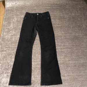 Svarta bootcut jeans - Svarta jeans med klassisk femficksdesign och bootcut-ben. Jeansen har normal midja och är tillverkade i ett mjukt denimtyg som ger en snygg passform. Perfekta för dig som gillar en tidlös och stilren look.