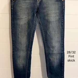 Blå jeans 28/32 - Säljer ett par jeans i klassisk blå tvätt med snygga slitningar och smal passform. Jeansen har fem fickor, dragkedja och är tillverkade i mjukt jeanstyg med lite stretch. Perfekta för en avslappnad och trendig look.