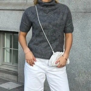 Grå polotröja i kashmir från Soft Goat - Mysig grå polotröja från Soft Goat i kashmir. Tröjan har korta ärmar och en hög polokrage, perfekt för lager på lager. Den är stickad och har en klassisk, enkel look som funkar till allt. Superskön och stilren för dig som gillar en clean vibe.