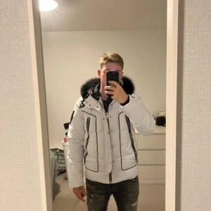 Vit pufferjacka från Horspist Paris - Säljer en snygg vit pufferjacka från Horspist Paris med svart fuskpäls på huvan och svarta detaljer vid dragkedjor och fickor. Jackan har emblem på ärmen, flera fickor och en chunky kedja på insidan. Perfekt för kalla dagar och riktigt stilren look.