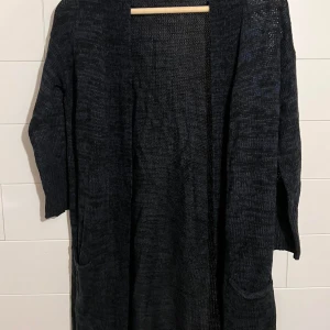 Blå lång kofta med fickor - Mysig blå lång kofta i stickat material med två stora fickor framtill. Perfekt att slänga på sig över en t-shirt eller hoodie för en chill look. Koftan har lång ärm och öppen front utan knappar eller dragkedja.