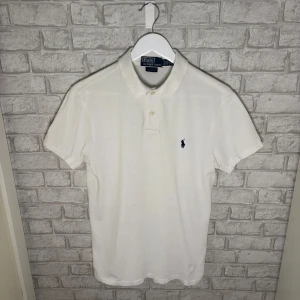 Ralph Lauren piké  - Ralph Lauren piké i klassisk modell och stilren vit färg. En tidlös och lättmatchad piké som passar perfekt till vardag och sommar. I bra skick, finns några små diskreta prickar framtill samt ett litet hål vid kragen bak enligt bild, inget som stör helhetsintrycket. Hör av dig vid intresse 🙌