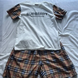 Burberry T-shirt och shorts  - Vit t-shirt från Burberry med klassisk logga framtill och korta ärmar i ikoniskt beige, svart och rött rutigt mönster. Rund halsringning och avslappnad passform. Perfekt för dig som gillar designer och vill sticka ut med coola detaljer.
