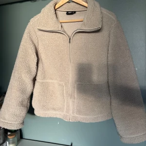 Beige teddyjacka med dragkedja - Supermjuk och fluffig teddyjacka i beige med hög krage och hel dragkedja framtill. Jackan har två stora fickor. Från lager 157 i storlek S, ordinarie pris 300 kr. Använd några få gånger i våras men är i ny skick. 