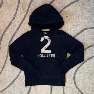 Mörkblå hoodie från Hollister - Mörkblå hoodie från Hollister med stor vit 2:a och broderad logga på bröstet. Tröjan är skit det och i svin bra kvalitet, materialet känns som nytt! Pris kan alltid diskuteras 