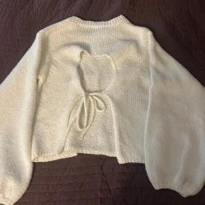 Vit stickad tröja med öppen rygg från NA-KD - Superfin vit stickad tröja från NA-KD i storlek M. Tröjan har långärmade puffiga ärmar och en croppad passform. Baksidan har en öppen rygg med ett hjärtformat hål och snörning som knyts. Perfekt för dig som gillar unika detaljer!💕