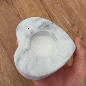 Ljushållare  - Bilderna visar en hjärtformad ljushållare i marmorliknande betong, med en urgröpning för ett värmeljus. Produkten har en modern, stilren design och är i gott skick med mindre naturliga märken i materialet. Perfekt som dekorativ detalj i hemmet.