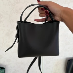 Svart handväska från ARKET i skinn - Svart handväska från ARKET i slätt skinn. Väskan är perfekt storlek för det viktigaste och passar till alla snygga outfits i höst😍. Väskan är använd ett fåtal gånger och priset går att diskutera!!😇