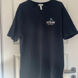 Svart t-shirt med tryck 'GET THE GOOD' - Svart t-shirt i bomull med vit text 'GET THE GOOD' tryckt på bröstet och ryggen. Klassisk rund hals och korta ärmar. Enkel och clean design med liten vågdetalj på framsidan. Perfekt för en chill och avslappnad stil. Säljer då den inte används!🥰