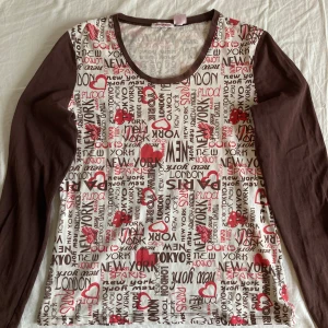 Brun långärmad tröja med tryck - Säljer en långärmad tröja med bruna ärmar och vit framsida med tryck i rött och brunt. Har en liten blekt fläck på baksidan av ena ärmen!