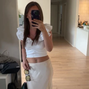 Vit volangtopp med breda axelvolanger - Supersöt vit topp från Zara med breda, lager-på-lager volanger över axlarna och croppad passform. Toppen är ärmlös och har lätt rynk framtill för en snygg siluett. Perfekt för dig som vill sticka ut med en feminin och trendig look.