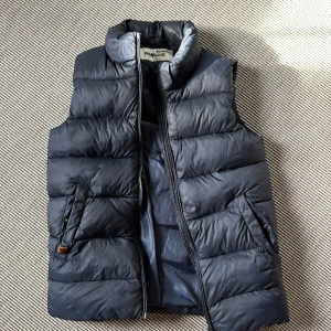 Pomp de Lux - Mörkblå dunväst - Snygg mörkblå dunväst från Pomp de Lux med hög krage och dragkedja framtill. Västen har två fickor med knappdetalj och är quiltad för extra värme. Perfekt för lager-på-lager under kyliga dagar. Stor i storleken. 