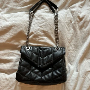 Svart quiltad axelväska med kedja - Snygg svart quiltad axelväska med silverfärgad kedjerem och mjukt skinnliknande material. Väskan har en adjustable axelrem så du kan ha den som axelväska eller crossbody. Perfekt storlek för skolan med också som fin väska💞❤️