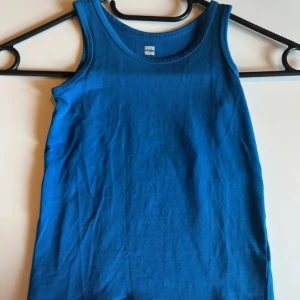 Blå linnetopp från HEMA - En enkel och stilren blå linnetopp från HEMA i storlek 110/116. Toppen är ärmlös med rund halsringning och tillverkad i mjuk bomull, perfekt för varma dagar eller som lager under andra plagg.