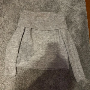 Grå offshoulder stickad tröja - Supermysig grå stickad tröja med bred offshoulder-krage och långa ärmar. Perfekt för kyliga dagar när du vill vara både varm och snygg. Ribbstickade detaljer vid krage, ärmslut och nederkant ger en extra touch.