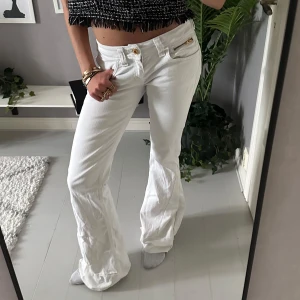Vita bootcut jeans med dragkedjor - Snygga omsydda vita jeans med bootcut passform, låg midja och guldiga dragkedjor på fickorna. 