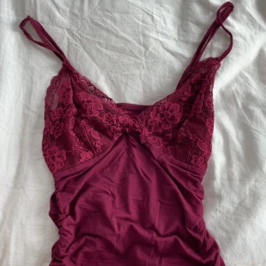 Vinröd spetslinnetopp med rosett - Supersöt vinröd linnetopp med tunna axelband och v-ringning. Överdelen är dekorerad med blommig spets och en liten rosett framtill. Har inga defekter och det helt oanvänd ut💕