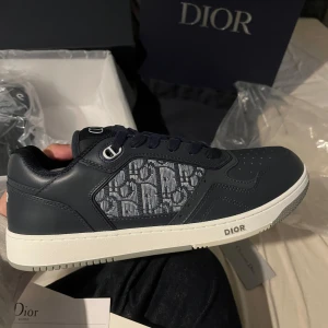 Dior skor - Snygga Dior skor i marinblått skinn med klassiskt Dior-mönster på sidan. Skorna har vit sula, snörning och diskreta logodetaljer på plös och häl. Perfekta för dig som vill ha en exklusiv och trendig look med lyxig känsla. Dom är oanvända köpte skorna på rea då retur inte går. Jag säljer skorna då de passar inte mig. Kvitto finns.