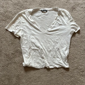 Vit v-ringad t-shirt från Zara - Vit t-shirt från Zara med v-ringning och korta ärmar. Tillverkad i mjuk bomull och har en avslappnad passform. Perfekt basplagg att styla till olika looks.