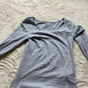 Grå långärmad topp från 157 - En basic grå långärmad topp från 157 med rundad halsringning. Tillverkad i en mjuk bomullsblandning med lite stretch för skön passform. Perfekt att styla med jeans eller kjol för en enkel och clean look.