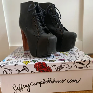 Jeffrey Campbell svarta Lita - Svarta boots från Jeffrey Campbell med kraftig platåsula och hög klack i trälook. Skorna har snörning framtill och en fyrkantig tå, vilket ger en edgy och cool vibe. Perfekta för dig som vill sticka ut och få extra höjd.