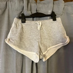 Grå sportiga shorts från new yorker - Snygga ljusgrå shorts från new yorker med vit kant och snörning i midjan. De har en sportig look och är tillverkade i mjuk bomull, perfekta för chill eller träning. Modellen är loose fit med rundade benkanter för en avslappnad vibe.
