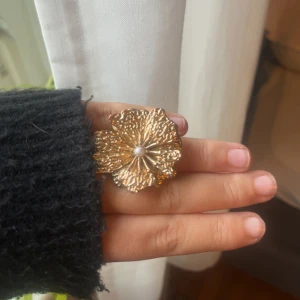 Guldig blomring med pärla - Unik ring i guldton med stor blomformad design och en liten pärla i mitten. Perfekt statement piece för dig som vill sticka ut och addera lite extra bling till din look!!