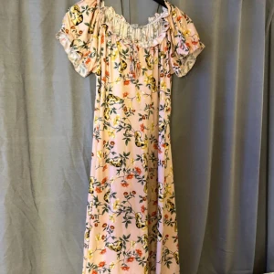 Blommig långklänning från Gilli - Superfin långklänning från Gilli i ljusrosa med blommigt mönster och gula detaljer. Klänningen har korta puffärmar, volang vid halsringningen och knyt fram. Perfekt för sommarens alla tillfällen och ger en romantisk vibe.