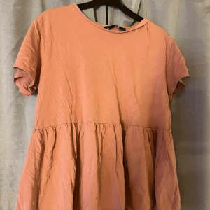 Rosa kort klänning från 157 - Supersöt rosa kortklänning från 157 med rund halsringning och korta ärmar. Klänningen har en avslappnad passform och volang nedtill som ger en skön och luftig känsla. Perfekt för varma dagar och enkel att styla med sneakers eller sandaler.