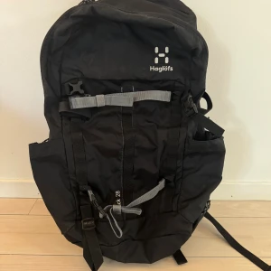 Svart ryggsäck Haglöfs Bäck 28L - Säljer en svart Haglöfs Bäck 28L ryggsäck med grå detaljer och flera smarta fack. Perfekt för dig som vill ha en stilren och funktionell väska med justerbara axelremmar och praktiska spännen. Rymmer mycket och passar till både skola och äventyr. Använd 1 gång 