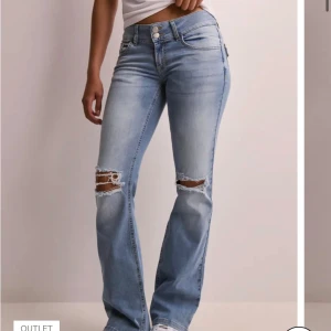 Ljusblå bootcut jeans med slitningar - Snygga ljusblå jeans med bootcut passform med slitna knän. Byxorna har låg midja, dubbla knappar och fickor med knapp bak. Säljer då dom är för långa på mig som är 155cm. Storlek 36 men skulle säga att dom passar 38 också då dom är stretchiga.