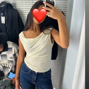 Kräm/vit top - En topp med tyg som hänger, det gör att tröjan går att bära på olika sätt.